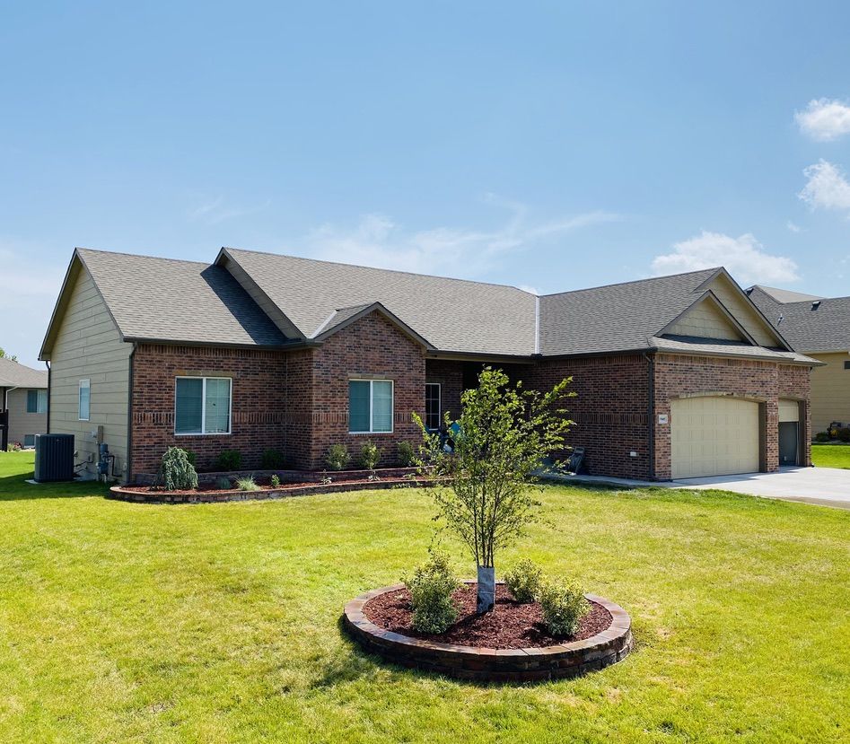 Brick home with new stone landscape beds along the house and a round tree bed in the lawn, installed by Leisure Lawn Solutions