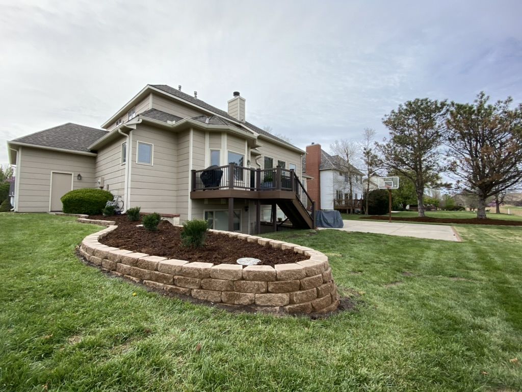 Curved raised stone bed with shrubs and mulch in the back yard near the deck