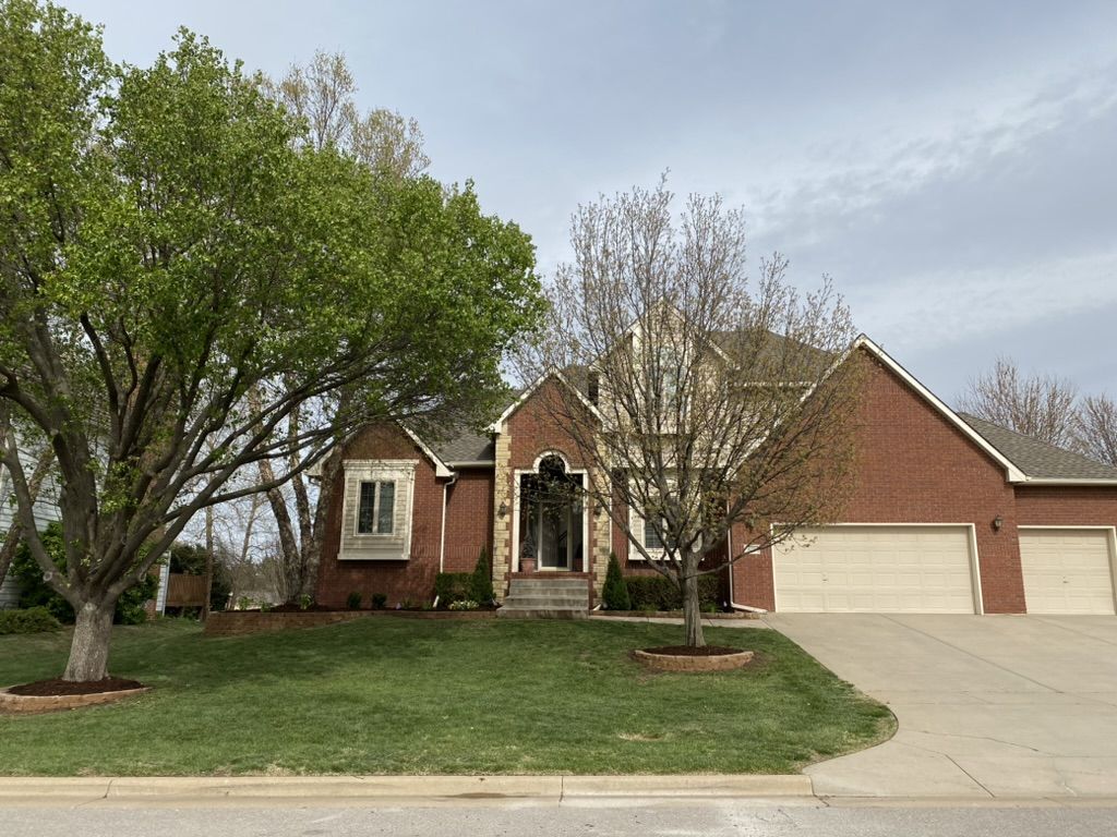 Front of a brick home with finished beds and stone tree rings in the lawn